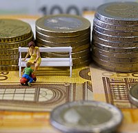 Eine miniatur Bank mit Mutter und Kind. Im Hintergrund gestapelte Geldmünzen.