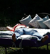 Ein Bett auf grüner Wiese. Darauf ruht sich ein Mensch aus.