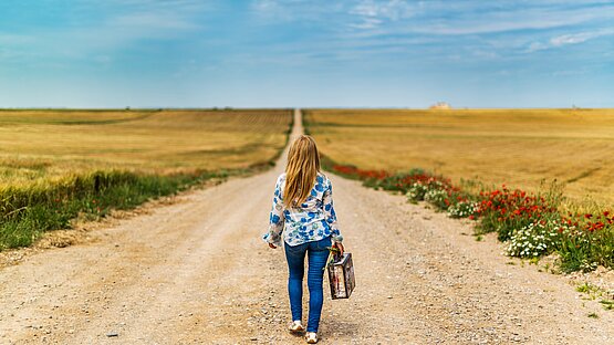 Eine Frau mit Koffer geht einen Langen Weg Richtung Horizont