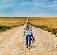 Eine Frau mit Koffer geht einen Langen Weg Richtung Horizont