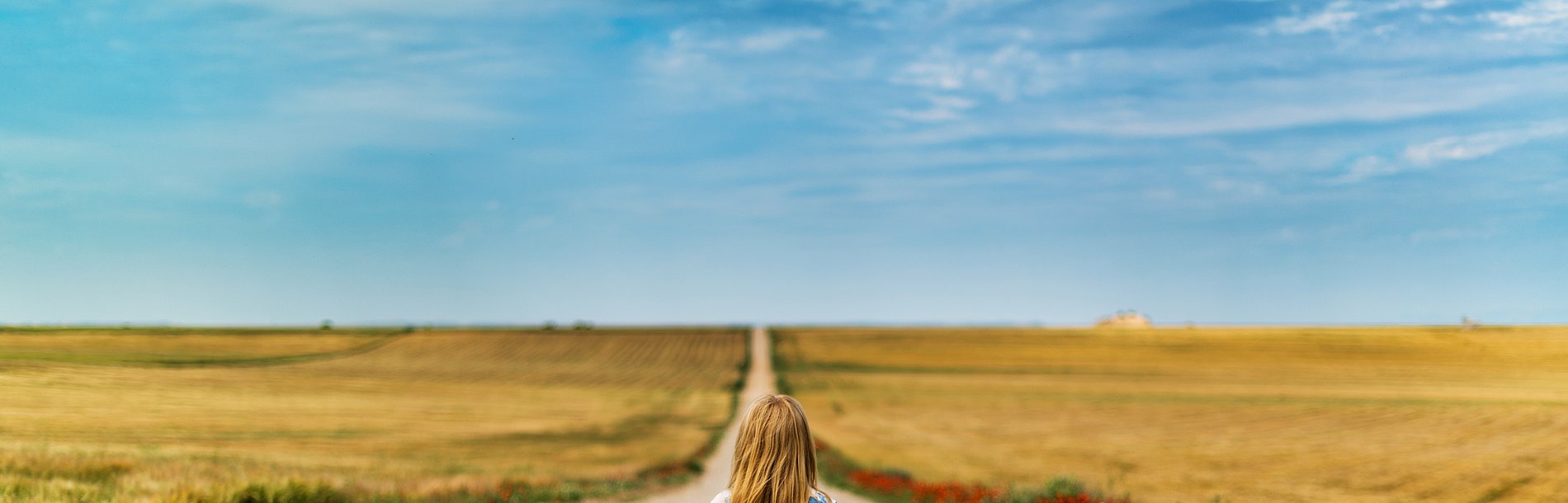 Eine Frau mit Koffer geht einen Langen Weg Richtung Horizont