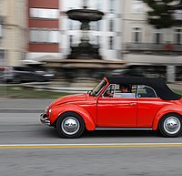 Roter VW Käfer fährt vor unscharfem Hintergund