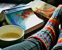 Entspannt hochgelegte Füße mit Socken neben Kaffee und Büchern auf Tisch.