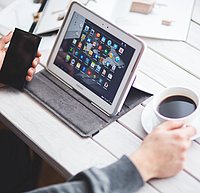 Mann sitzt am Tisch mit Tablet Handy und einer Tasse Kaffee